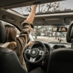 A young woman enjoying a drive with the sunroof open, showing car interior detail.