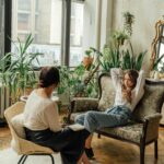 Two women engaged in a counseling session in a cozy, plant-filled living room.