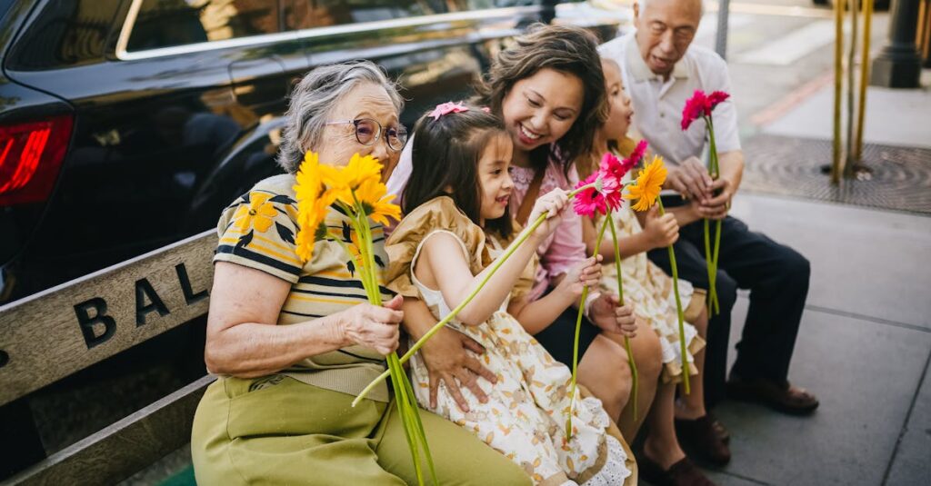 Happy multigenerational Asian family sitting together with flowers on a city bench, enjoying a sunny day.