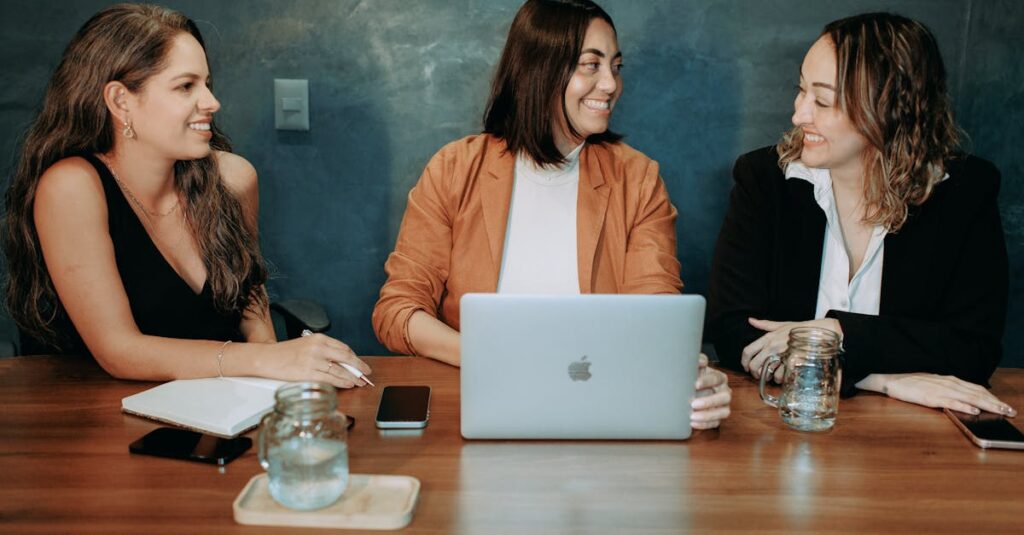 Three women engaged in a professional meeting with a laptop and notes, fostering teamwork and collaboration.