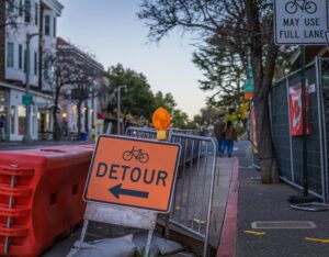 Street scene featuring a bicycle detour sign and metal railings, guiding traffic.