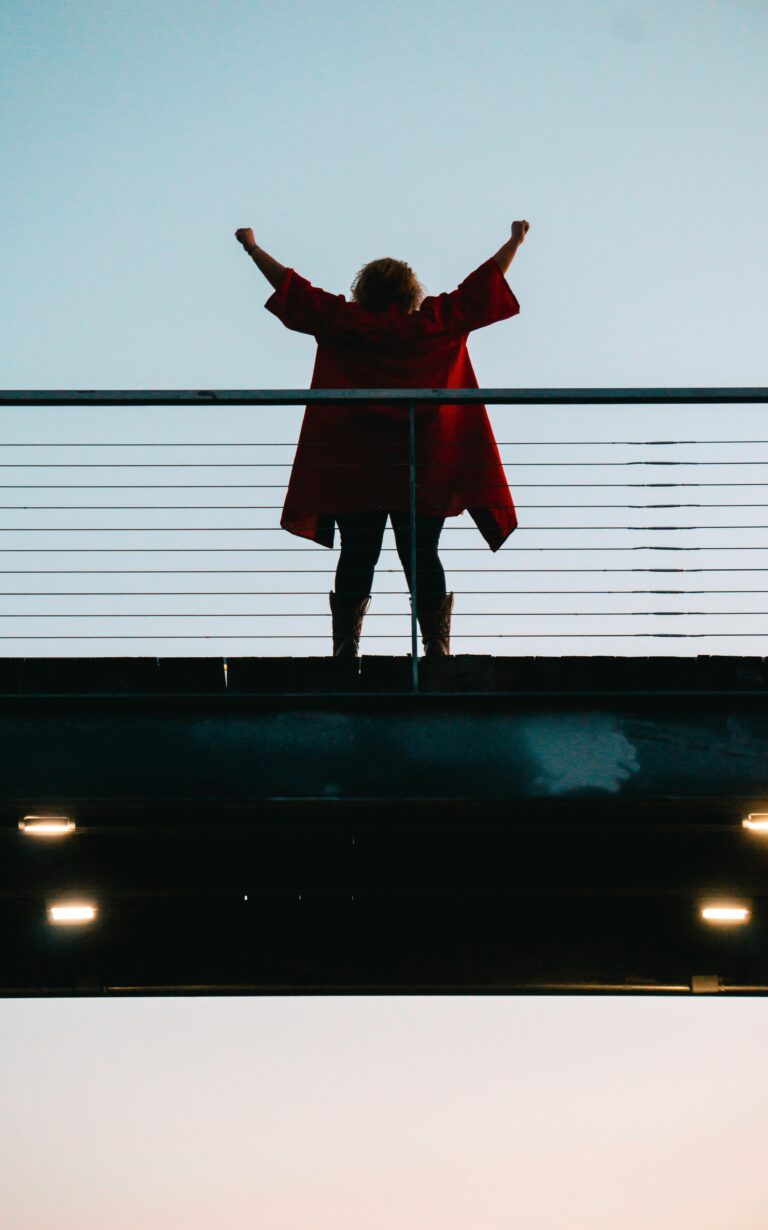 Back view of a woman with raised arms, celebrating on a bridge at dusk.