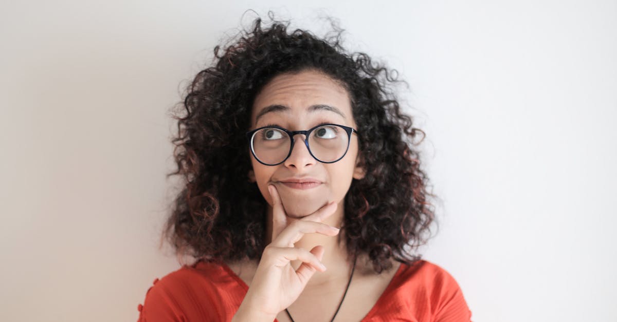 Portrait of a thoughtful woman in a red top, with curly hair and glasses against a white background.