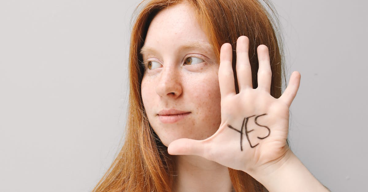 Confident woman shows 'Yes' written on her hand with a grey background.