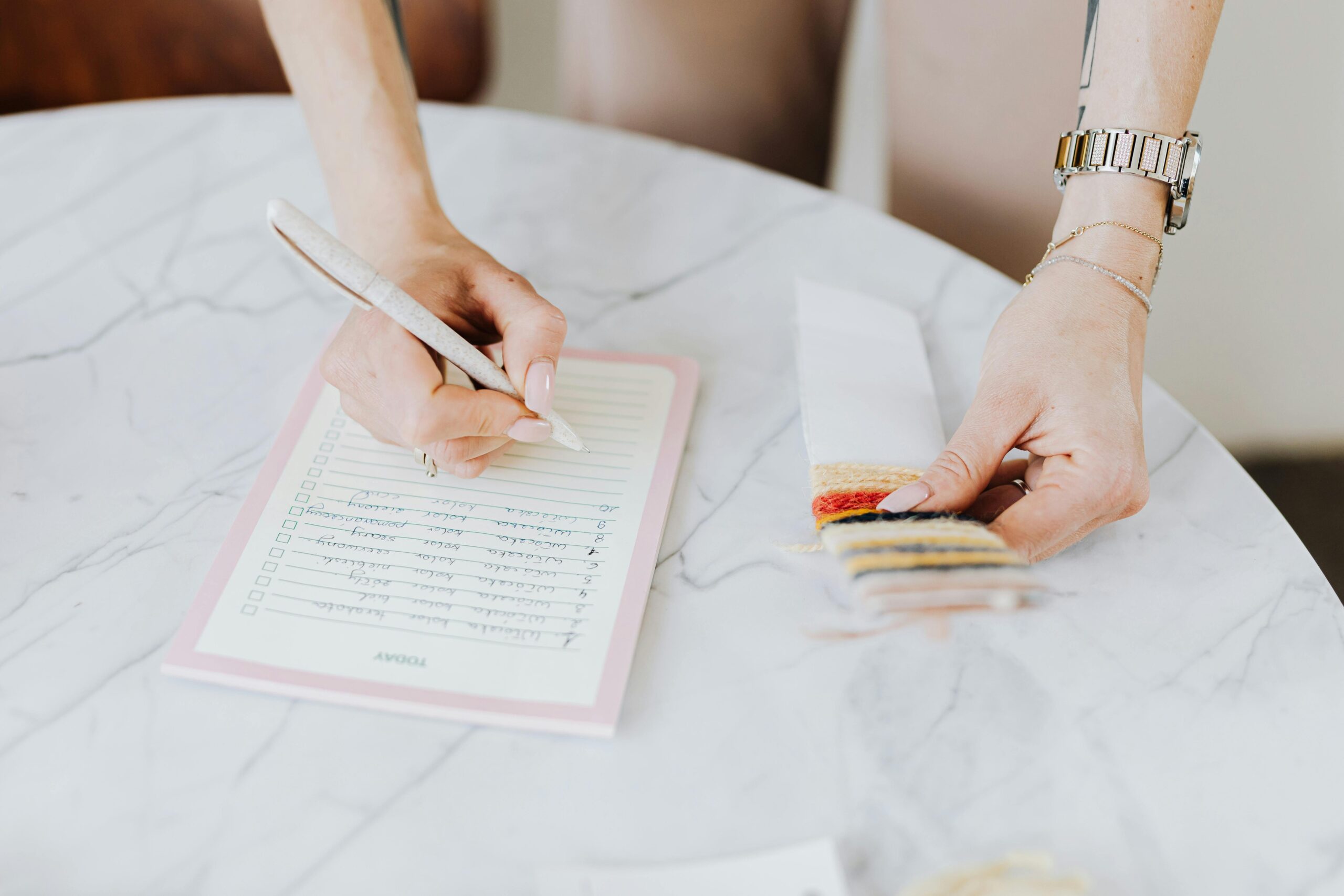 Close-up of a woman organizing fabric samples and writing notes on a marble table.