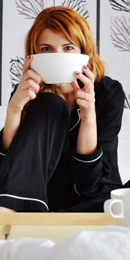 A woman enjoys a cup of coffee in a stylish and cozy bedroom, perfect for relaxation.
