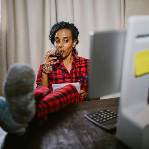 Woman in red pajamas relaxing with wine at a home office desk with feet up.
