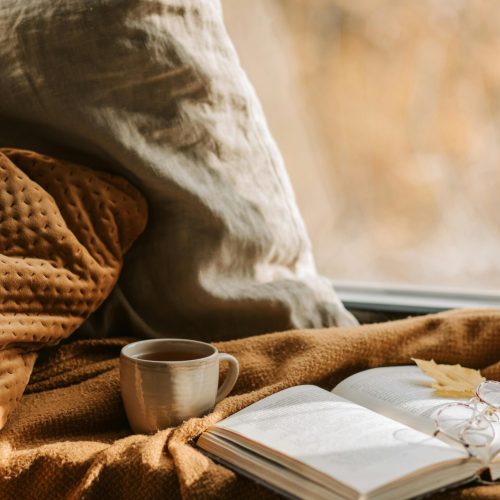 Inviting autumn scene with book, eyewear, and a warm drink by a window, perfect for relaxation.